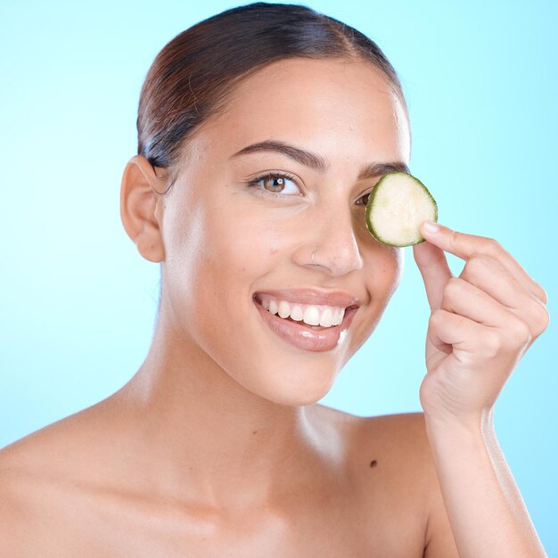 Pepino para el cuidado de la piel y retrato de belleza de mujer sobre dermatología natural cosmética facial Persona feliz con producto de spa vegetal para el cuidado de la piel brillo y bienestar facial sobre fondo azul