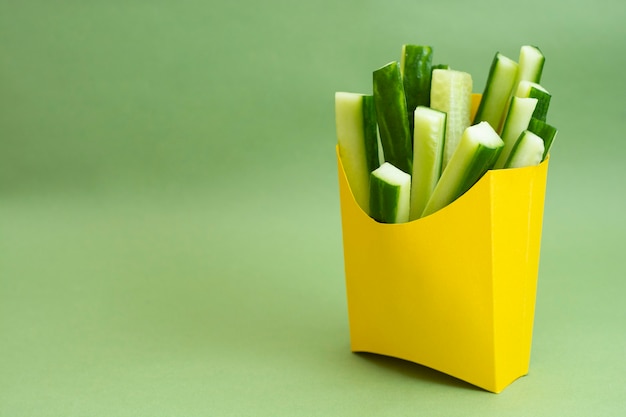 Pepino fresco em palitos de lanche em uma caixa de papel amarela sobre fundo verde