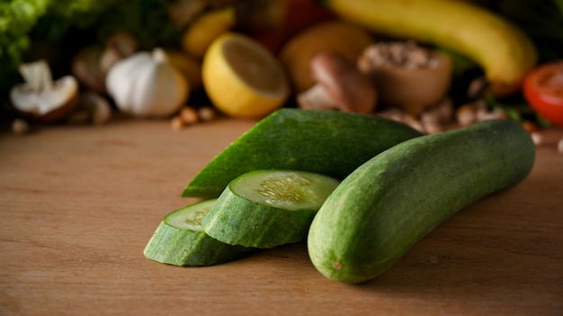 Pepino fresco y toboganes de pepino sobre mesa de madera con verduras y frutas en segundo plano.