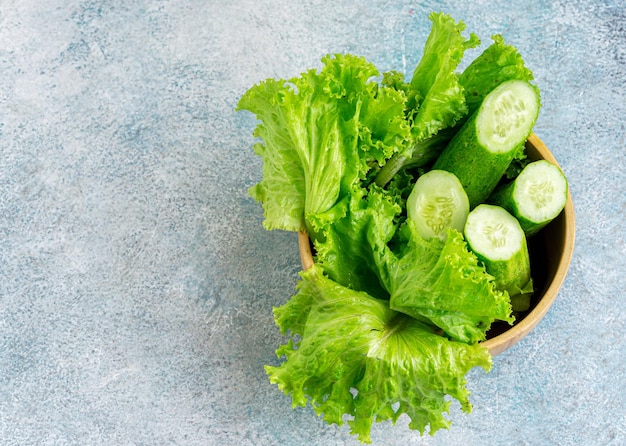 Pepino y lechuga en un cuenco de madera y fondo azul.