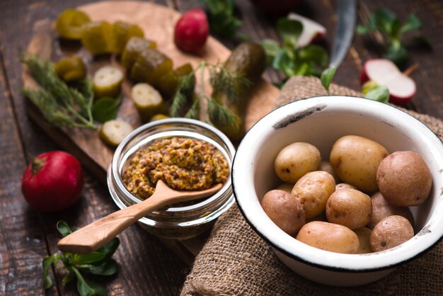 Pepino, rábanos, lechuga, mostaza en un recipiente sobre una tabla para cortar