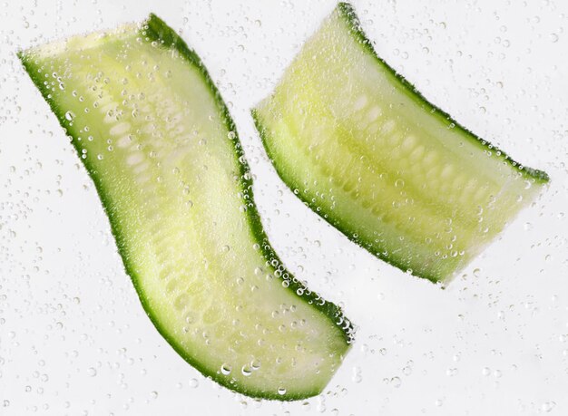 Pepino en rodajas con burbujas de agua sobre fondo blanco Concepto de cosméticos hidratantes para la piel