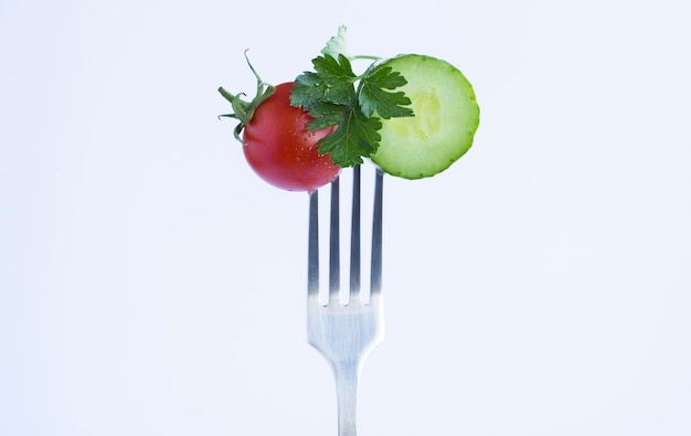 Pepino de tomate cherry y perejil apuñalados en un tenedor de plata sobre el fondo blanco Espacio de copia de primer plano
