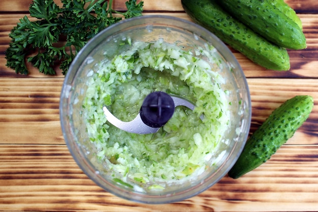 Foto pepino verde fresco picado no liquidificador em pequenos pedaços para cozinhar. vista superior de uma xícara com uma massa. vegetais deliciosos e saudáveis.