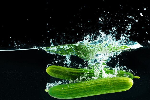 Pepinos cayendo al agua con un toque contra el negro