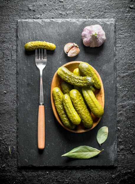 Pepinos conservados el plato en un tablero de piedra con la hoja de laurel y el ajo