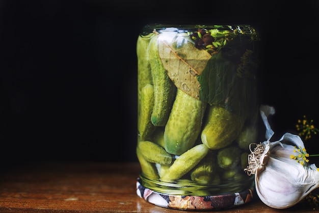 Pepinos em conserva em uma jarra de vidro com alho e endro em um fundo escuro