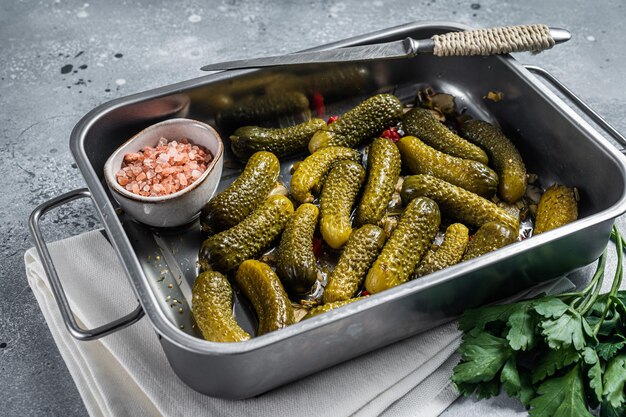 Pepinos en escabeche marinados caseros con eneldo, ajo y especias en bandeja de cocina grande. Fondo gris. Vista superior.