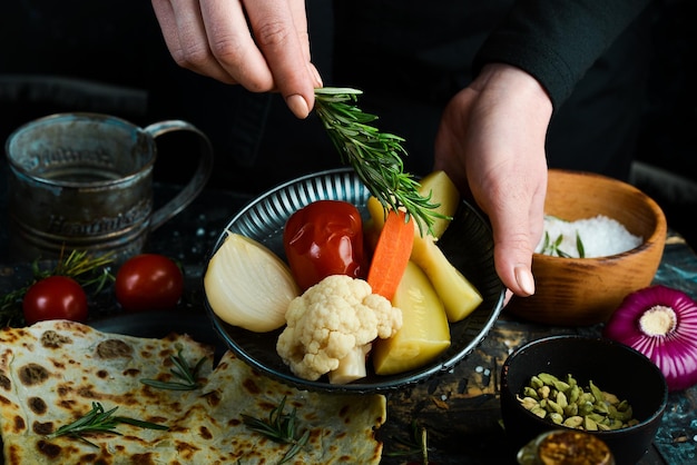 Pepinos en escabeche tomates cebollas y repollo en un plato en manos de un chef sobre un fondo negro