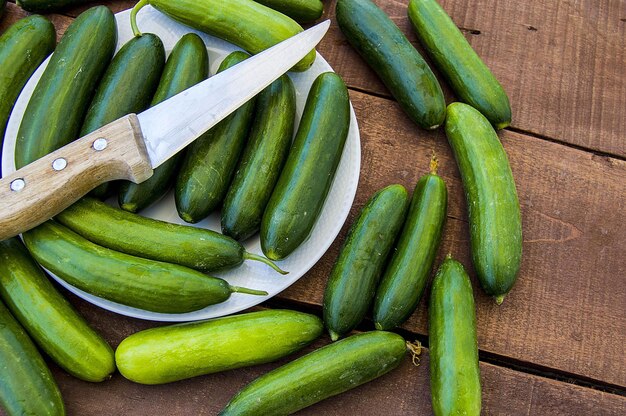 Pepinos de jardín natural listos para ser picados con un cuchillo uno al lado del otro en el suelo de madera