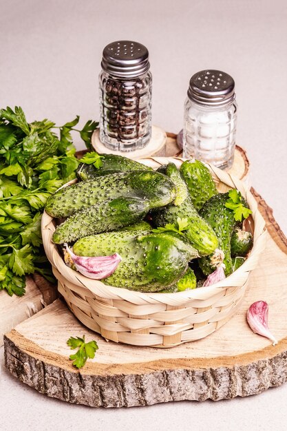 Pepinos orgánicos feos de moda en una canasta. Verduras frescas, dientes de ajo, mostaza, perejil, especias. Soporte de madera, luz dura moderna, sombra oscura. Fondo de hormigón de piedra, espacio de copia