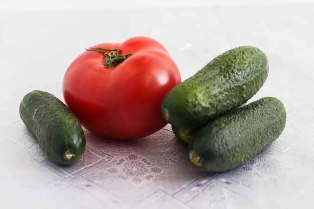 Unos pepinos y un tomate sobre un mantel blanco.