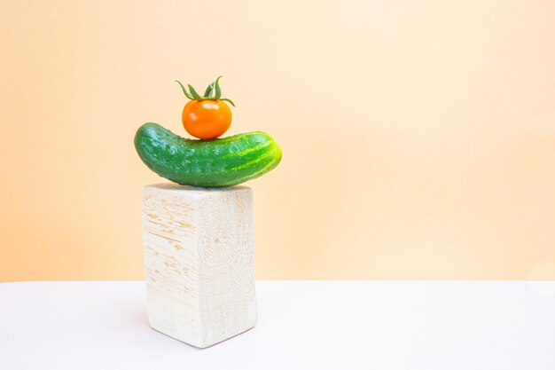 Pepinos y tomates frescos en podios de madera en un espacio de luz neutra. Concepto de cosecha de vegetales, alimentos orgánicos saludables. Minimalismo, espacio de copia.