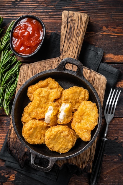 Pepitas fritas de frango de fastfood em uma panela Fundo de madeira Vista superior