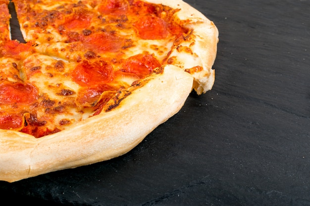 Pepperoni oder Diabola Pizza mit Salami, Chili Pepper, Mozzarella Käse, Kirschtomaten, Tomatensauce auf schwarzem Hintergrund Nahaufnahme.