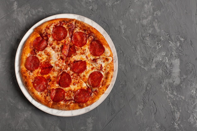 Pepperoni-Pizza auf grauem Betonhintergrund mit Kopienraum. Draufsicht der geschnittenen Peperoni-Pizza.