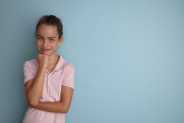 Pequeña adolescente emocional con camisa rosa de 11 a 12 años sobre un fondo azul aislado Retrato de estudio de los niños Coloque el texto para copiar el espacio para la publicidad de subtítulos de los productos de los niños