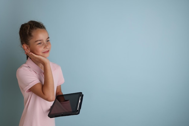 Pequeña adolescente emocional con camisa rosa de 11 a 12 años sobre un fondo azul aislado con una tableta en las manos Retrato de estudio de los niños Coloque el texto para copiar el lugar de la inscripción