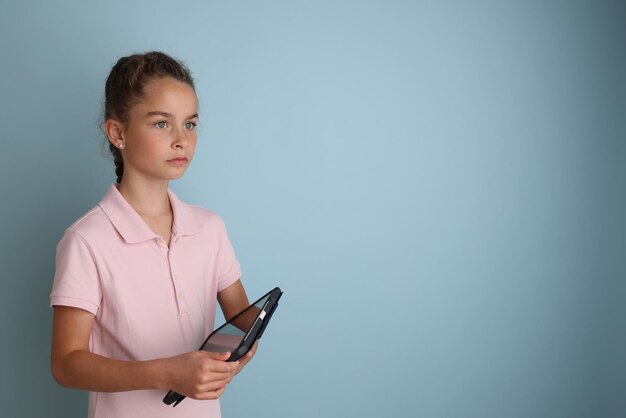 Pequeña adolescente emocional con camisa rosa de 11 a 12 años sobre un fondo azul aislado con una tableta en las manos Retrato de estudio de los niños Coloque el texto para copiar el lugar de la inscripción