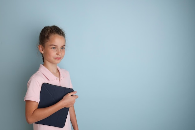 Pequeña adolescente emocional con camisa rosa de 11 a 12 años sobre un fondo azul aislado con una tableta en las manos Retrato de estudio de los niños Coloque el texto para copiar el lugar de la inscripción
