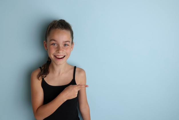 Pequeña adolescente emocional con una camiseta negra de 11 12 años sobre un fondo azul aislado Retrato de estudio de los niños Coloque el texto para copiar el lugar de la inscripción