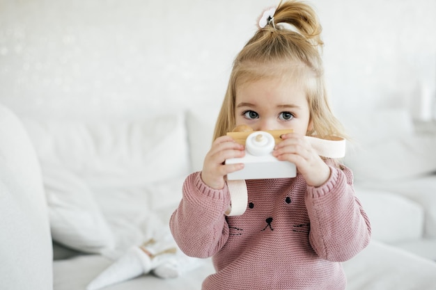 Pequena adorável garota segurando a câmera de brinquedo de madeira