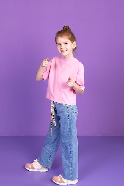 Una pequeña y alegre niña rubia feliz sonriente sostiene sus brazos cruzados doblados de forma aislada en un retrato de estudio infantil de fondo púrpura El concepto de estilo de vida en la infancia