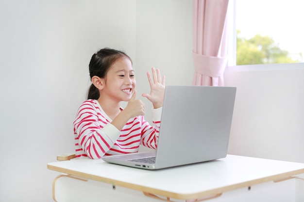 Pequena aluna asiática estudando aula de aprendizagem on-line por videochamada no laptop