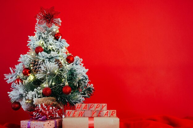 Pequena árvore de Natal decorada com presentes e mensagem de feliz ano novo Copie o espaço no fundo vermelho