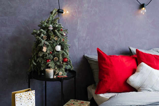 Pequena árvore de natal na mesa de cabeceira e presentes perto da cama em quarto elegante