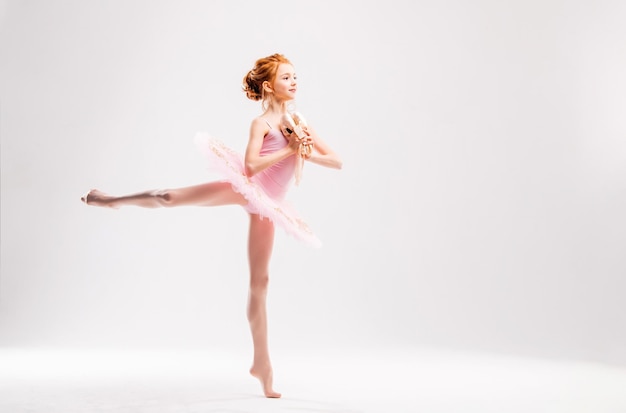 Pequeña bailarina bailarina en una academia de tutú rosa posando sobre un fondo blanco