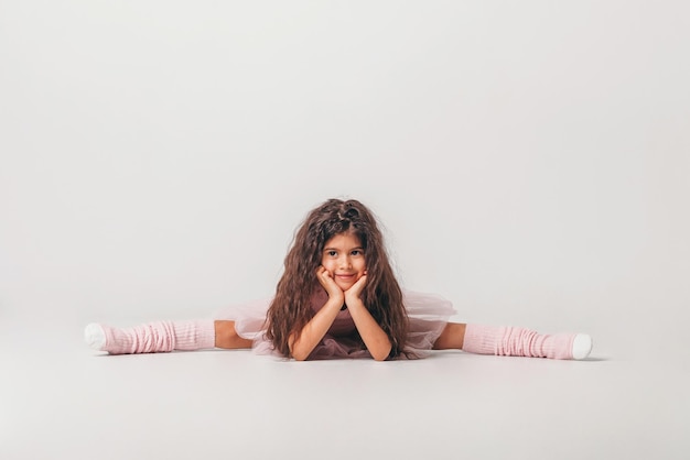 Pequeña bailarina morena en un estudiante de la academia de tutú rosa posando sobre fondo blanco