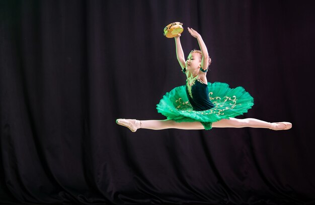 Pequeña bailarina que se congela en el salto en el escenario en tutú con zapatos de punta con una pandereta, una variación clásica de Esmeralda.