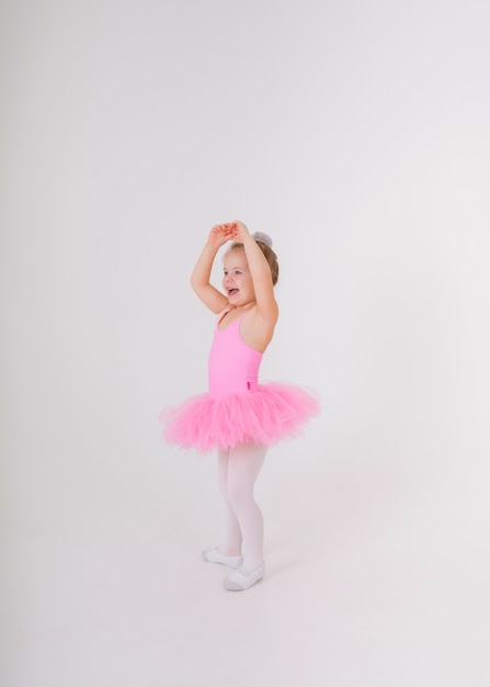 Pequeña bailarina rubia en un vestido de tutú rosa baila en una pared blanca