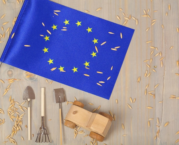 Pequeña bandera de la Unión Europea y granos de avena, herramientas agrícolas, tractor de juguete de madera sobre una superficie de madera. Espacio libre para un texto