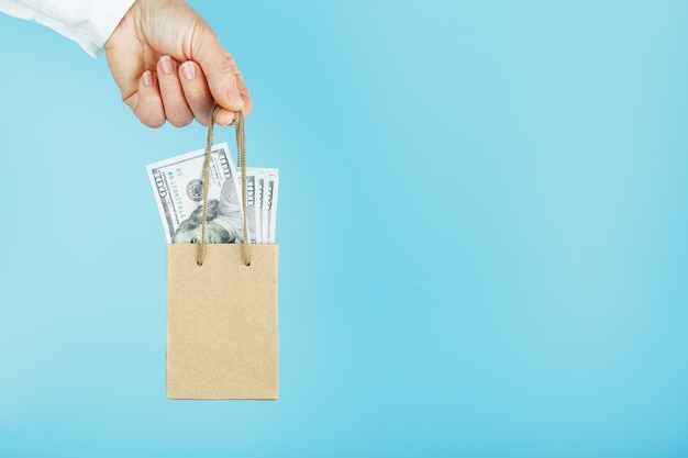 Una pequeña bolsa de papel para ayuda financiera y soporte hecha de papel con los dólares estadounidenses sobre un fondo azul. El concepto de apoyo financiero insignificante en los negocios,