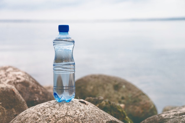 Foto pequeña botella de agua sobre la piedra del océano en el paisaje natural