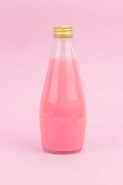 Foto pequeña botella de vidrio con una bebida de leche rosa sobre una pared rosa