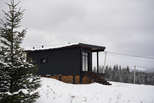 Pequena cabana de madeira preta moderna na floresta de pinheiros nevados