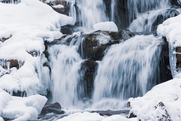 Pequena cachoeira de água fria flui entre as pedras cobertas de neve