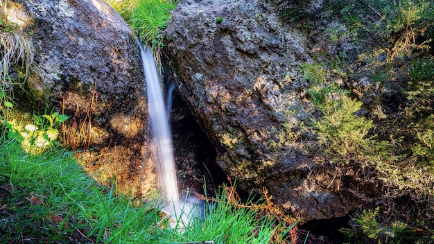 Pequena cachoeira entre rochas na montanha com plantas verdes e longa exposição.