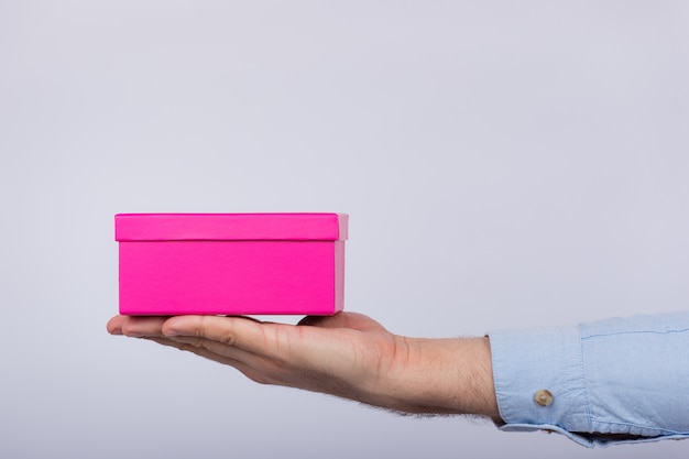 Foto pequena caixa rosa na mão de caras. homem segurando a caixa de presente. vista lateral