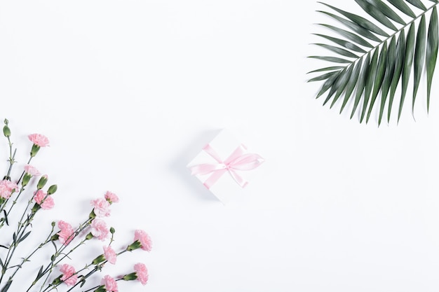 Pequeña caja con cinta rosa y flores sobre una mesa blanca
