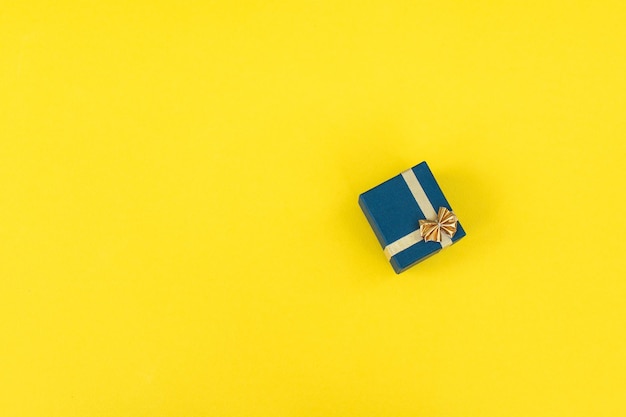 Una pequeña caja de regalo con una cinta dorada y un lazo sobre un fondo amarillo