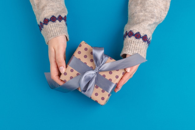 Pequeña caja de regalo en manos femeninas en azul, vista desde arriba