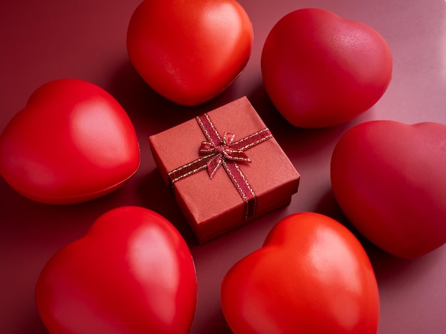 Una pequeña caja de regalo roja con cinta rodeada de muchas bolas de corazón sobre fondo rojo. Un regalo esencial en días especiales con amor, cumpleaños, Año Nuevo, Día de San Valentín y aniversarios.