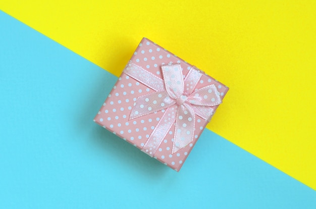Pequeña caja de regalo rosa en papel azul y amarillo pastel.