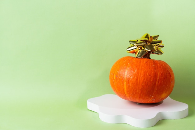 Pequeña calabaza naranja sobre fondo verde con espacio de copia. Celebración del concepto de Halloween o Acción de Gracias. Podio de cosméticos para halloween. Bodegón de otoño.