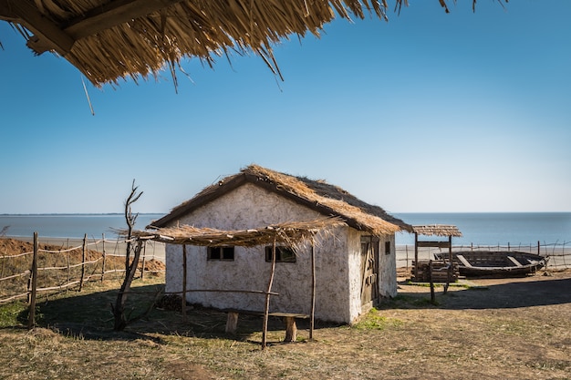 Pequeña casa antigua, pozo de madera y un barco agujereado a la orilla del mar