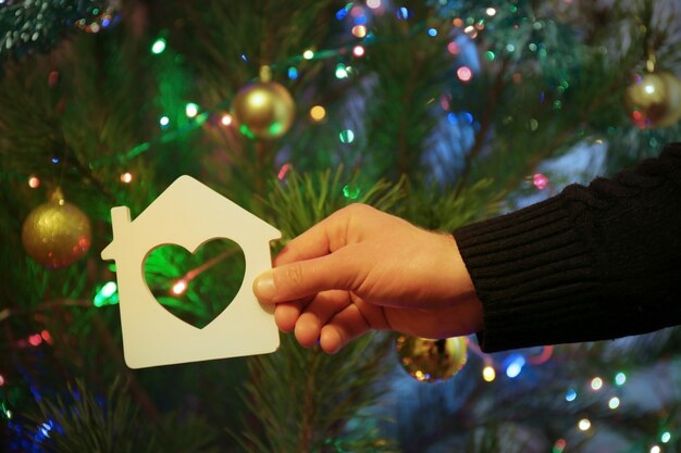 Pequeña casa con corazón en la mano del hombre sobre fondo de Navidad